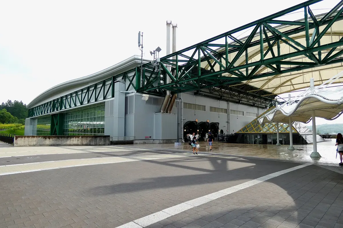 The long grey and green building that houses Ghibli's Grand Warehouse, with its glass entrance arches and a white canopy over the plaza in front