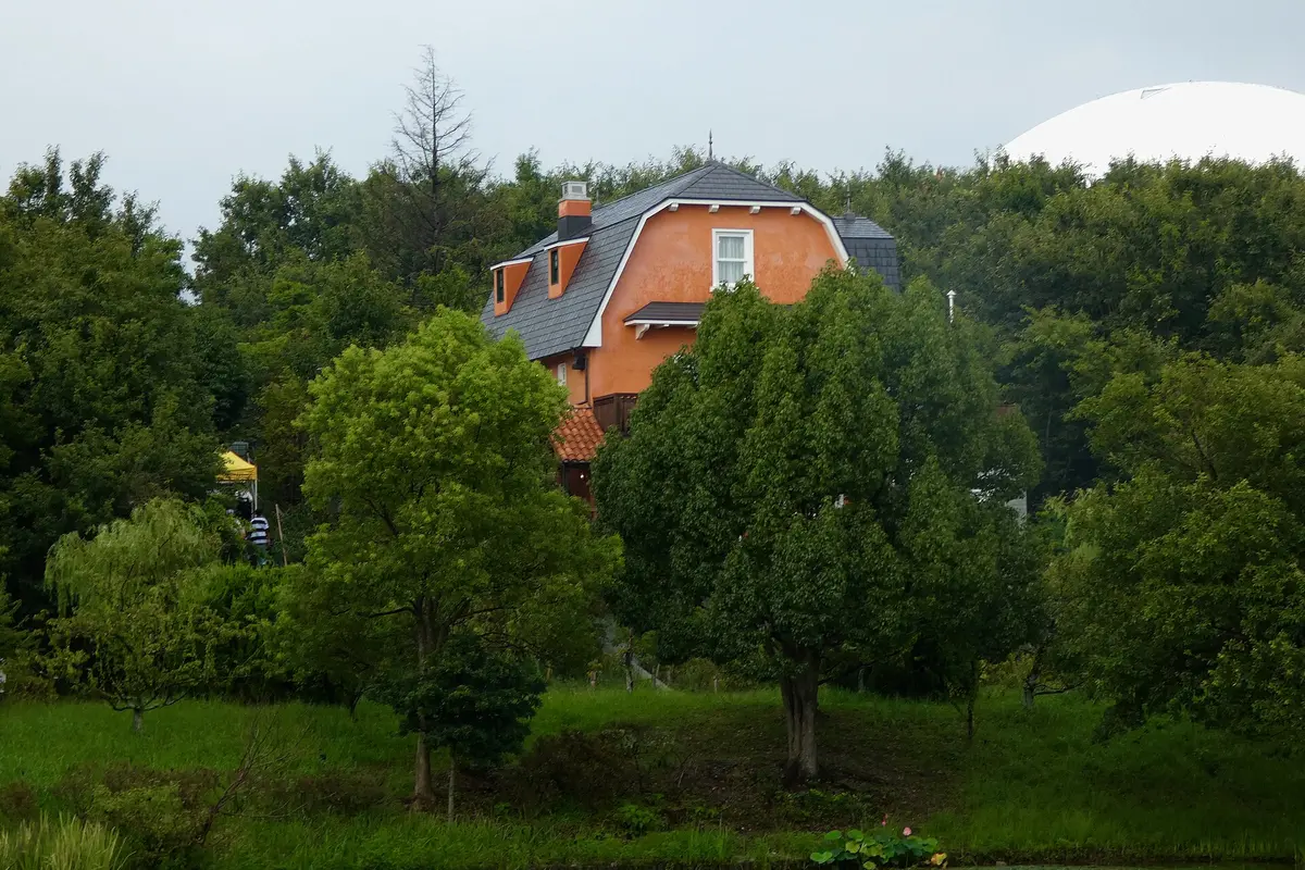 The World Emporium, an orange house with a steep grey roof, rising above the trees of Hill of Youth, with a white dome behind